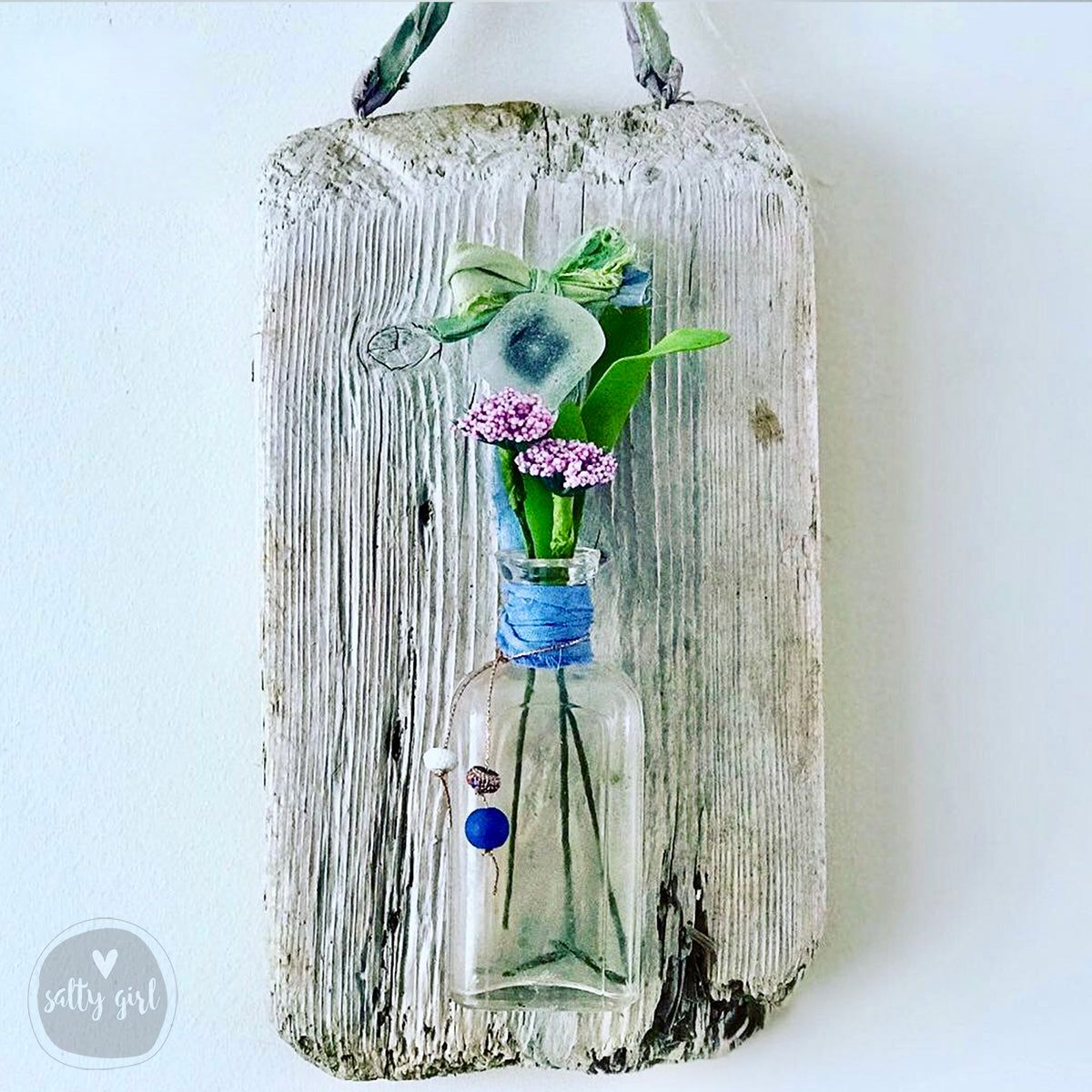 Handcrafted with Maine driftwood, an antique bottle and sea glass or beach stone knob, this precious wall vase will add a touch of the coast to any beach cottage or New England style home. Adorned with sari ribbon, color-coordinated beads, and faux flowers these antique bottle vases make a great friend gift, a one-of-a-kind wedding gift, house warming gift, or realtor's closing gift. Maine Driftwood, Driftwood Signs, Driftwood Wreath, Driftwood Wall Art, Driftwood Crafts, Seashell Crafts, Hanging Wall Vase, New England Style Homes, Green Knobs