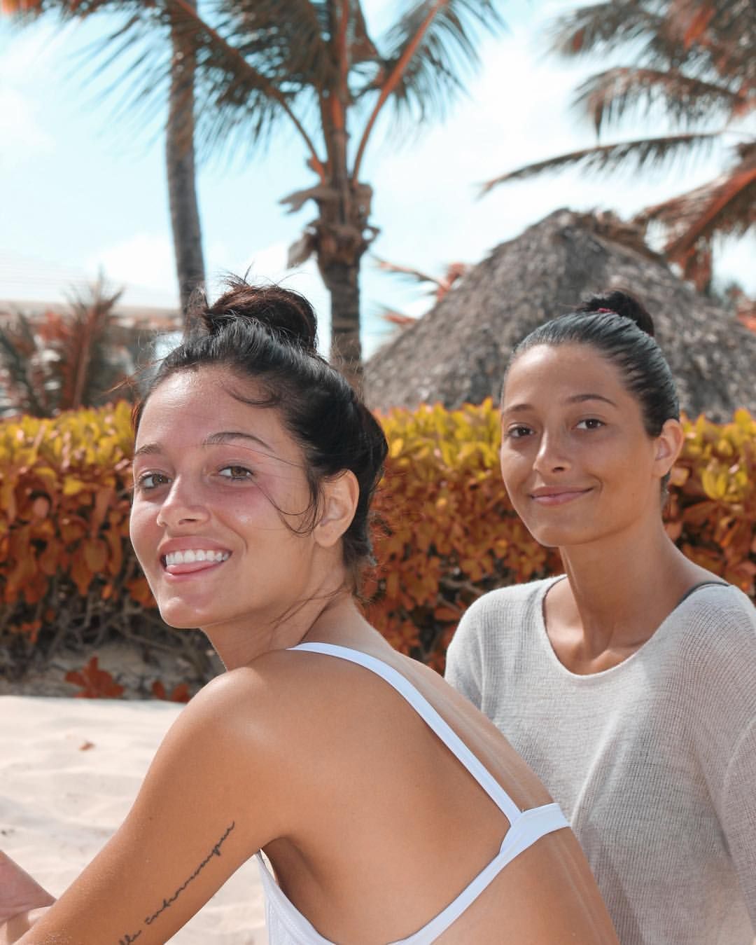 two women standing next to each other on a beach with palm trees in the