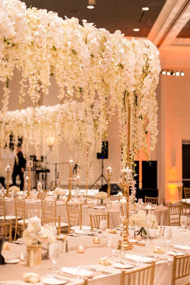 Luxury wedding tablescape | Hanging flower tall wedding centerpiece with white orchids and wisteria | A White And Gold Opulent Wedding Where Syrian Traditions Met Luxury Romance - Photographer: Julia Franzosa #table #tablesetting #tablescape #tabledecor #centerpieces #centerpieceideas Gold Wedding Centerpieces, Tall Centerpieces, Wedding Flower Arrangements, Wedding Table Centerpieces, Reception Decorations, Hanging Flowers Wedding, White Wedding Flowers Centerpieces, Masquerade Centerpieces, White Centerpiece