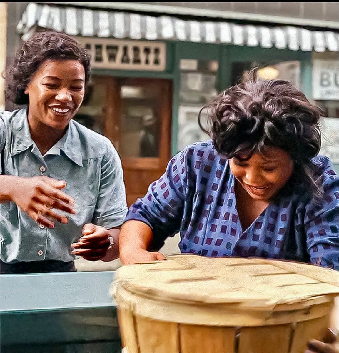 two women sitting at a table with a large wooden drum in front of them